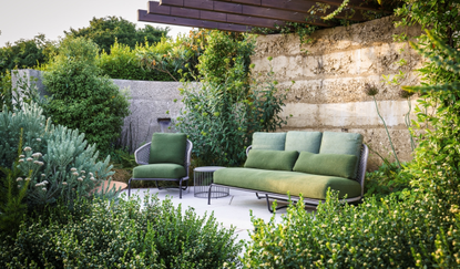 Green outdoor sofa and armchair in a rustic coastal garden with lush planting