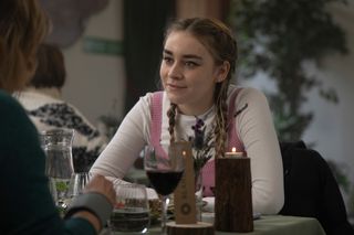 Morgan Strandhed (Silvie Furneaux) sits at a restaurant table, gazing intently at someone sitting just off-camera