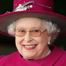 Queen Elizabeth wearing a magenta hat and coat looking excited