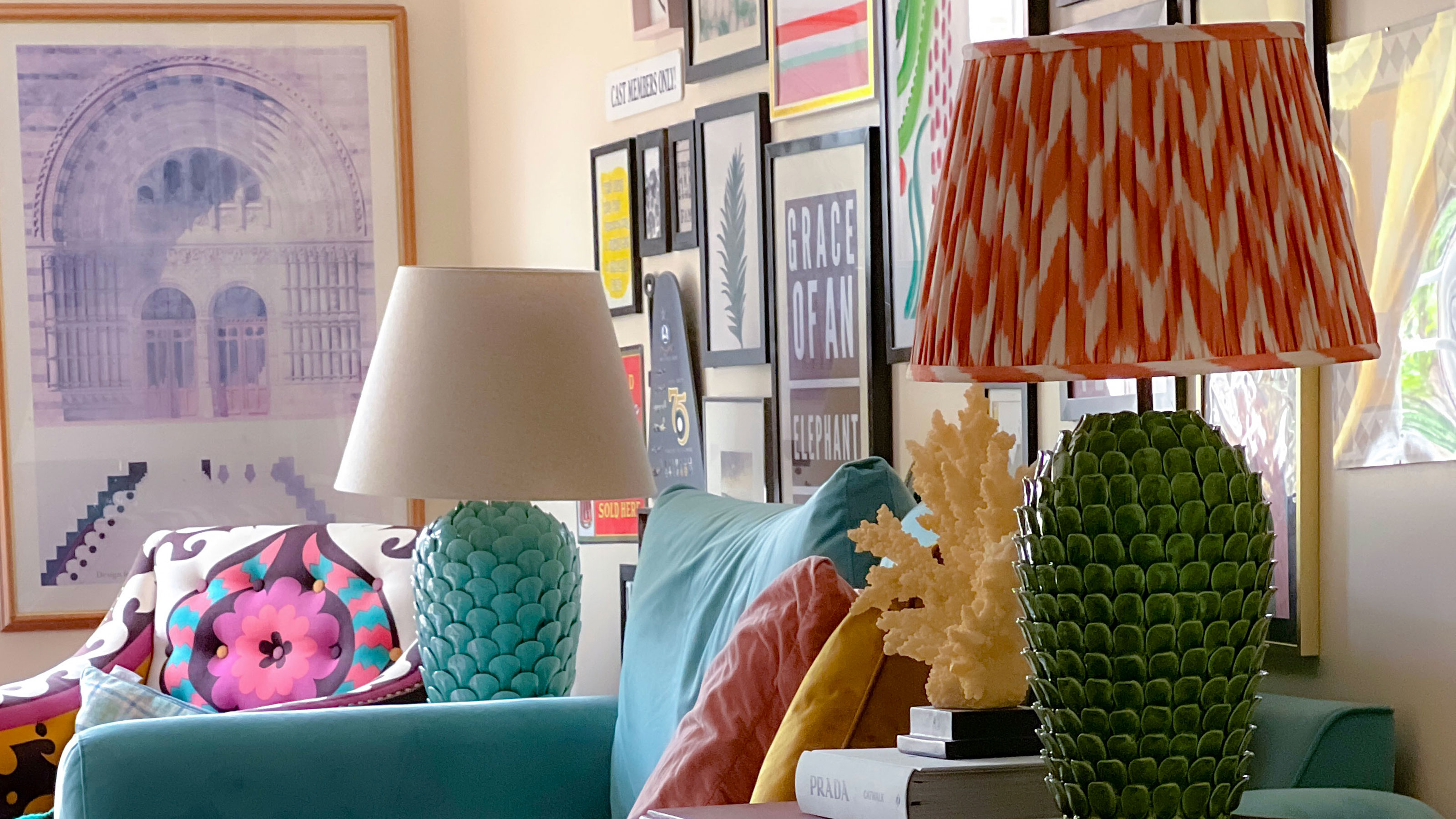 Living room with colourful gallery wall and teal sofa with a lamp on either side, one turquoise base with white shade, the other with a green base and orange chevron patterned shade