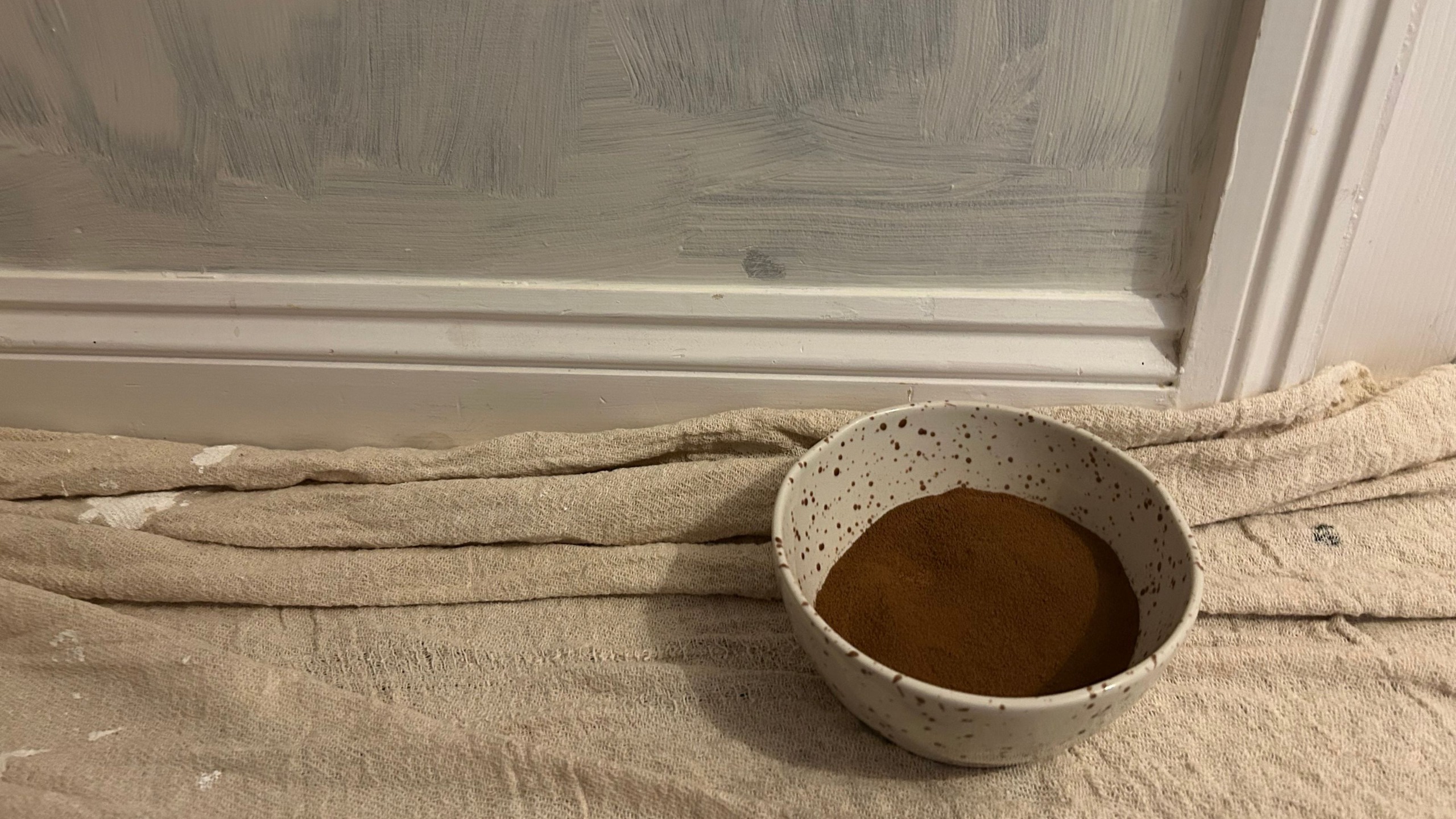 Ground coffee in a bowl on floor on dust sheet around painted wall