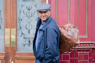 George Knight wearing a flat cap and carrying a brown leather bag outside the Vic in EastEnders.