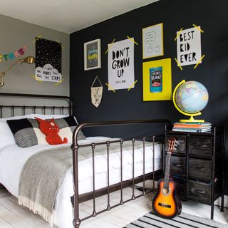 boys bedroom with black painted gallery wall, wooden floor and wrought iron bed