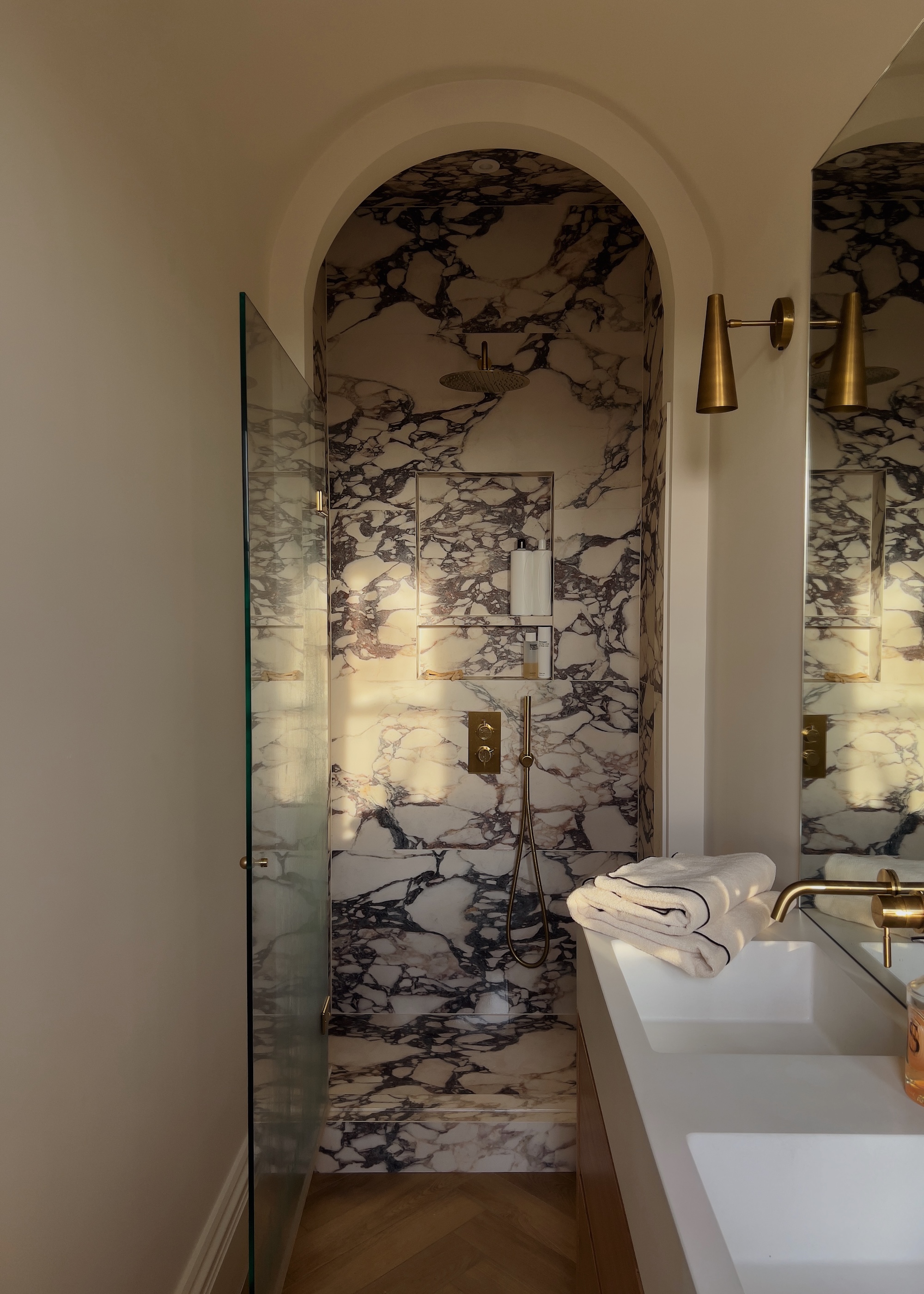 A marbled shower with an arched doorway and a double sink on the right side of the bathroom.
