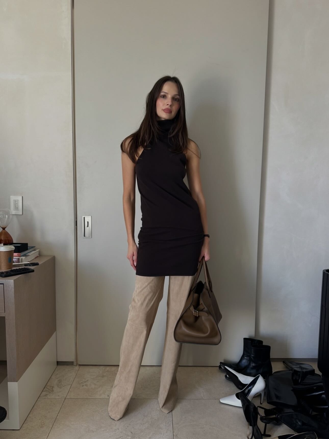 Pia Mance wearing a black top, tan suede pants, and a brown The Row Margaux bag.