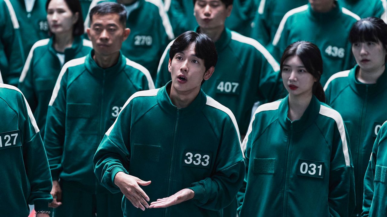 A group of people wearing identical green tracksuits with numbers printed on them, in &#039;Squid Game&#039; season 2.