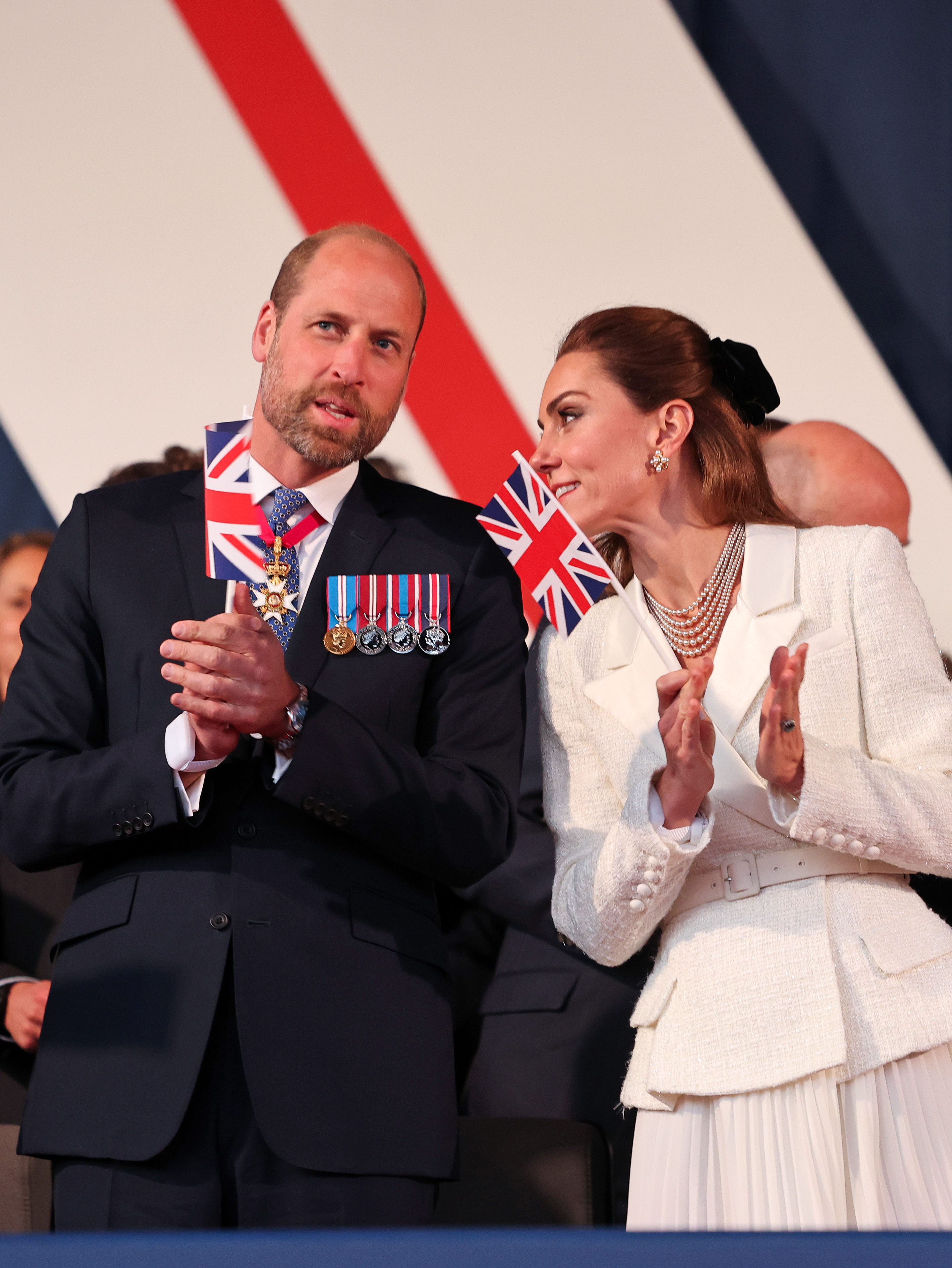 Kate Middleton wearing a white tweed blazer dress talking to Prince William at a VE Day anniversary concert