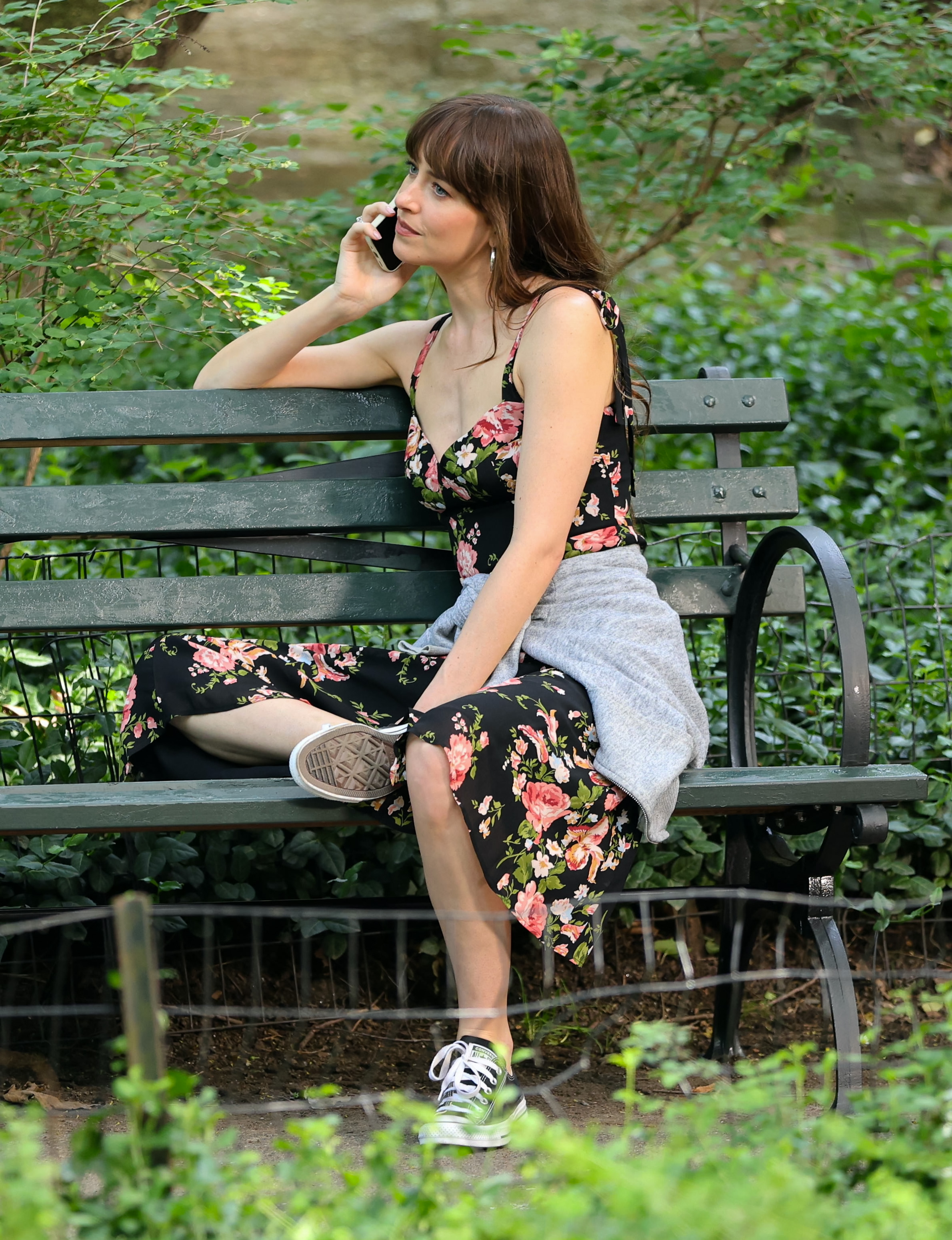 Dakota Johnson on a park bench wearing a Reformation dress and Converse
