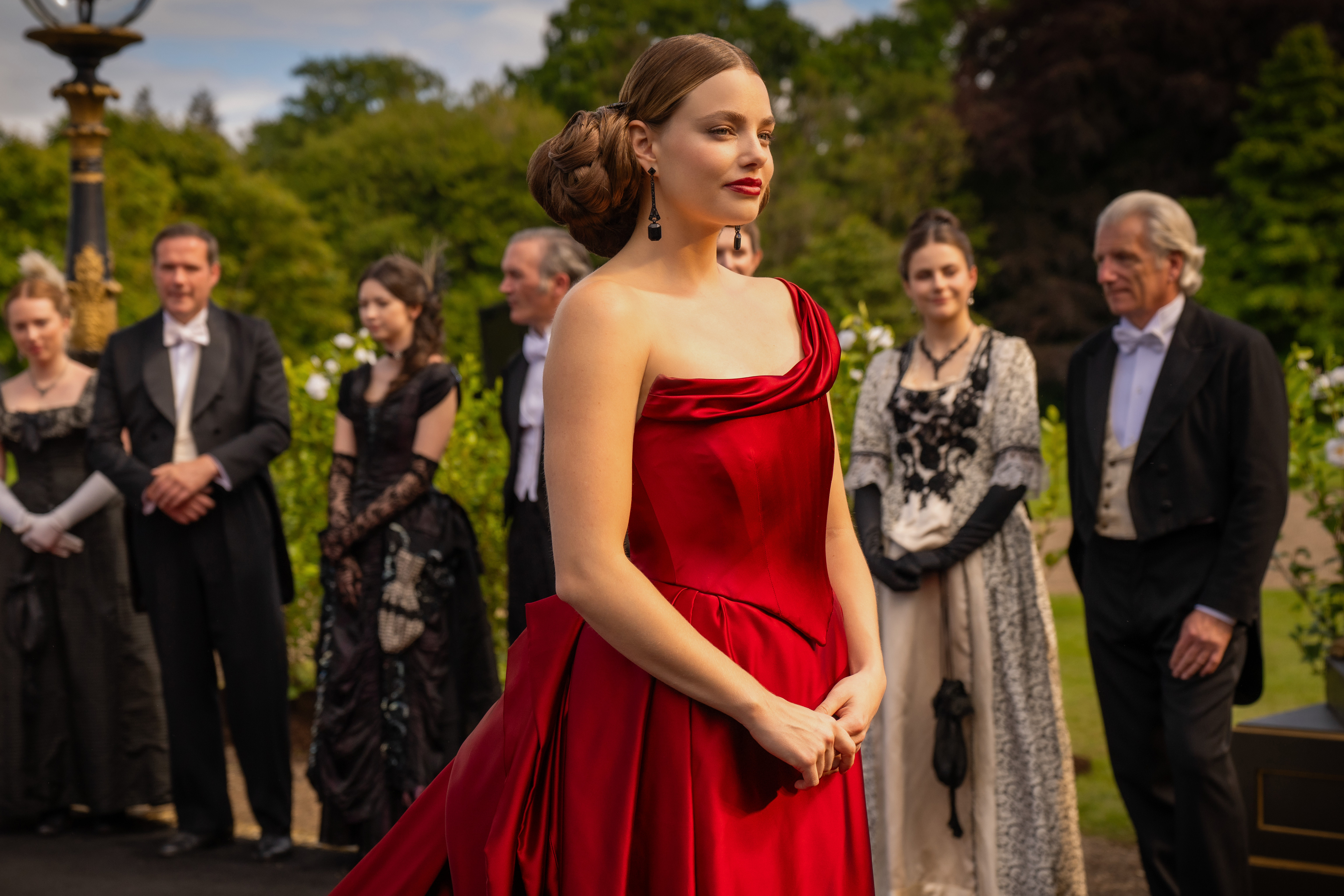 kristine froseth as nan wearing a red ball gown at a garden party in the buccaneers season 2