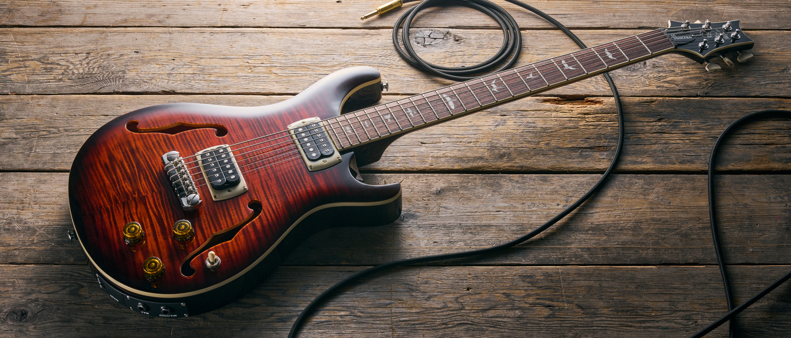 A PRS SE Ed Sheeran Hollowbody I Piezo Baritone lying on a wooden floor with a guitar cable trailed nearby