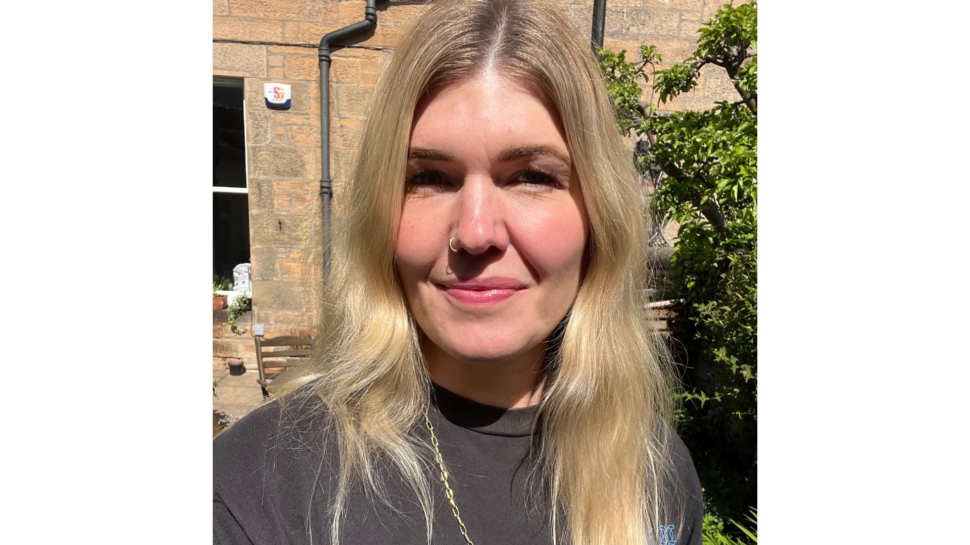 Fiona smiling with wavy long blonde hair and wearing the Merit Uniform Tinted SPF