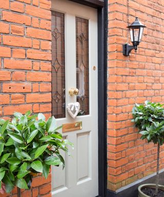 A white front door with a heart decoration on it, with brick walls either side and two green topiary plants either side too