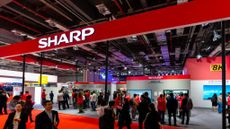 A red banner sign displaying the word Sharp suspended above a trade conference floor