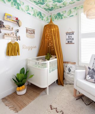 A baby boy nursery idea with cacti wallpaper on the ceiling and a mustard yellow canopy adorned with string lights.