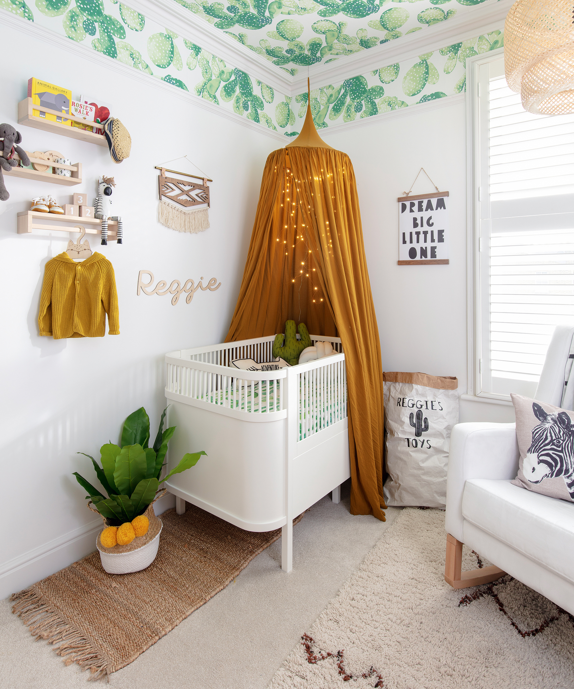 A baby boy nursery idea with cacti wallpaper on the ceiling and a mustard yellow canopy adorned with string lights.