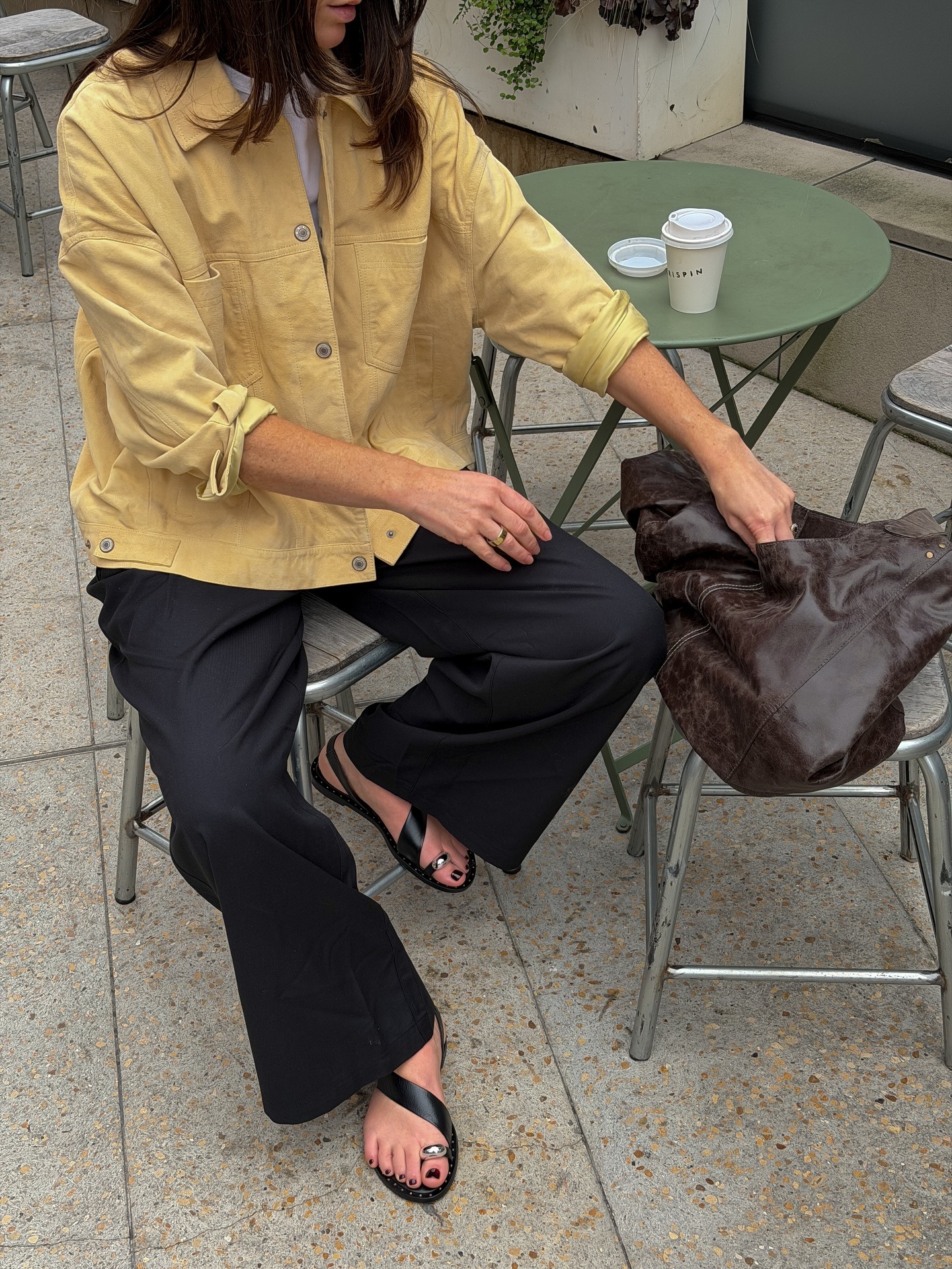 Woman wears yellow jacket, black trousers and metal hardware sandals