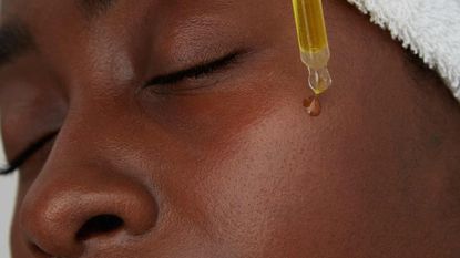 A close up of a young woman applying a skincare product on her face using a pipette