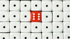 Stacks of white dice showing a single dot surround one red die with a six on it.