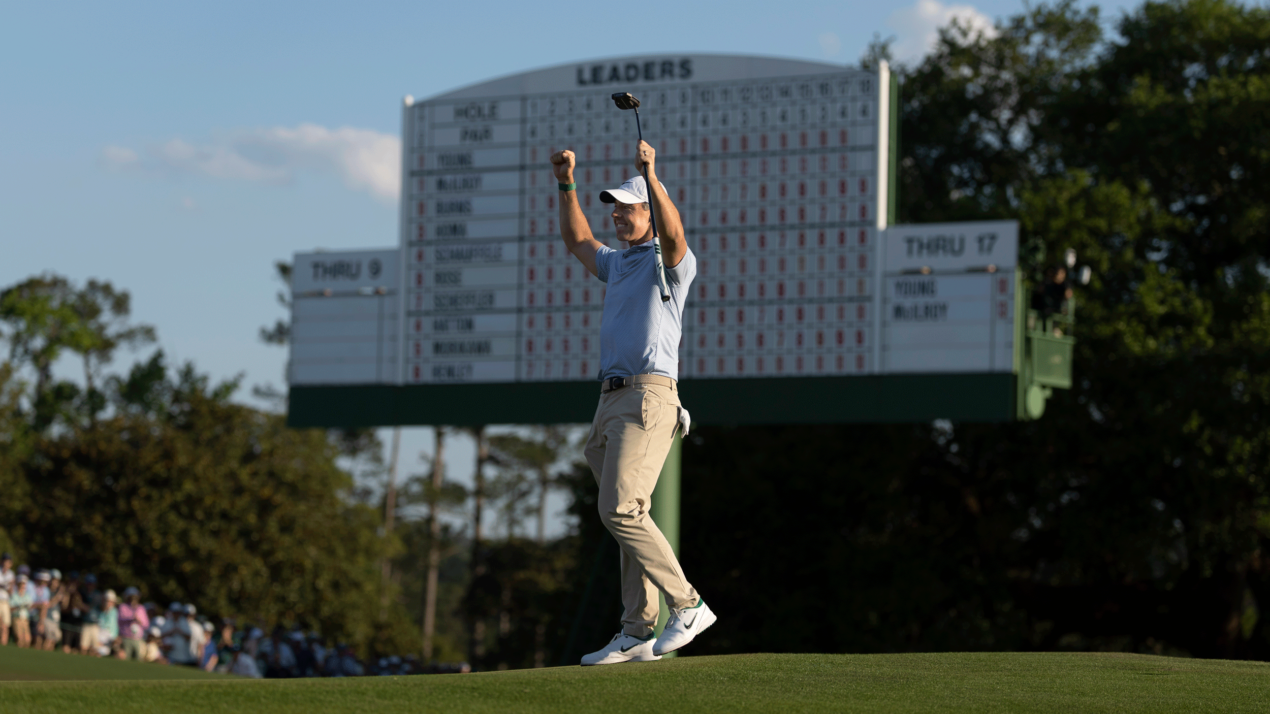 Rory McIlroy puts his two fists in the air to celebrate winning The Masters in 2026 with a giant leaderboard in the background