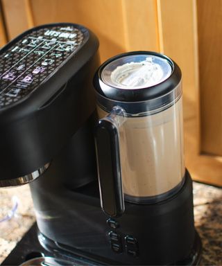A close-up of the Mr. Coffee® Single-Serve Frappe™, Iced, and Hot Coffee Maker blender with light wood cabinetry in background