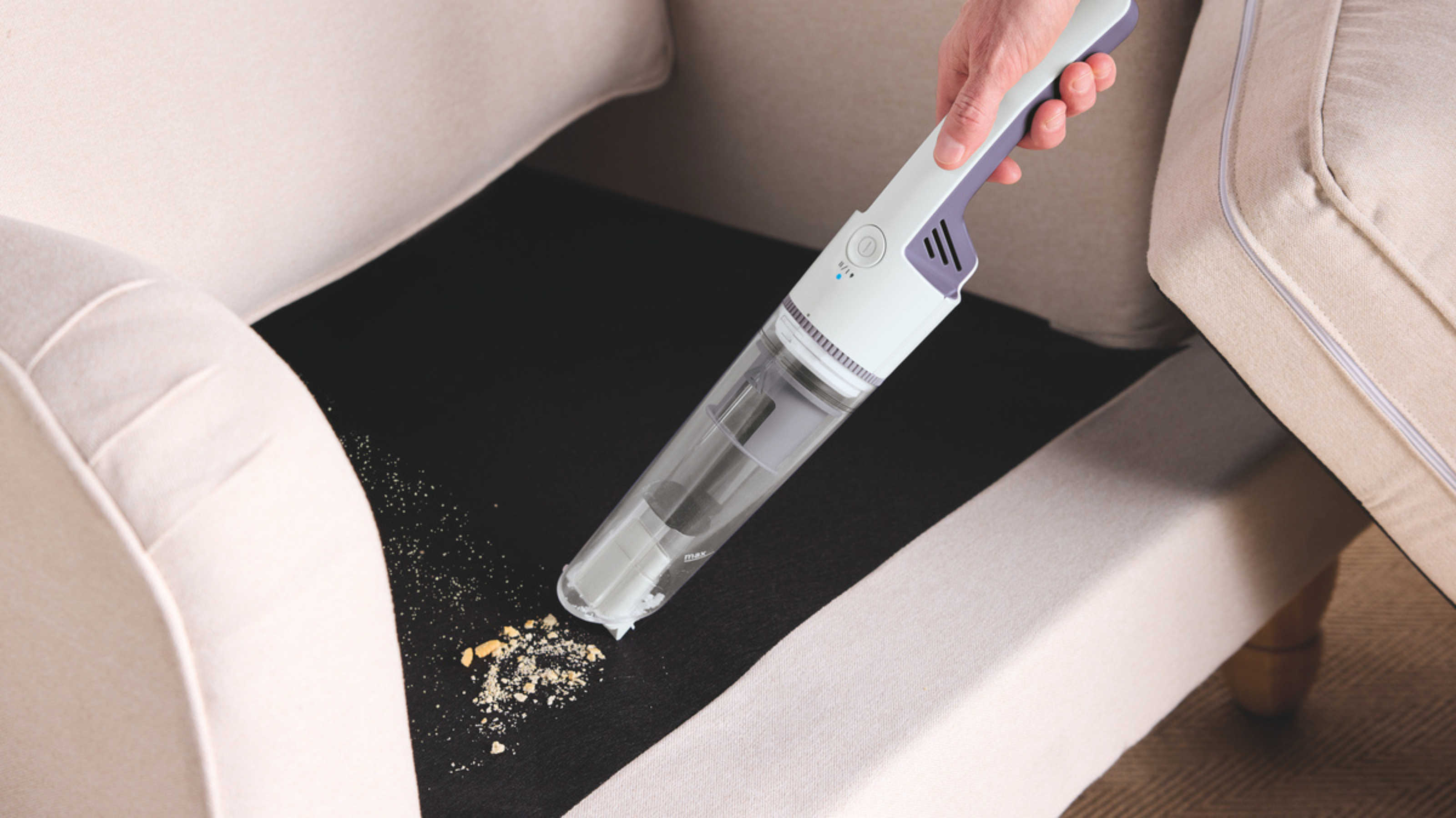 Aldi handheld vacuum being used to hoover crumbs from a sofa.