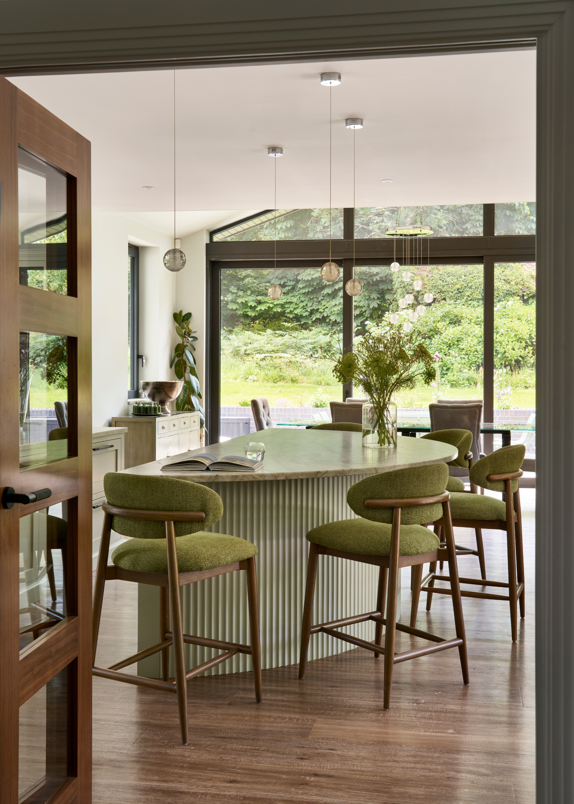 A tonal green kitchen with fluted island front in sage green, and bar chairs in olive green and dark wood