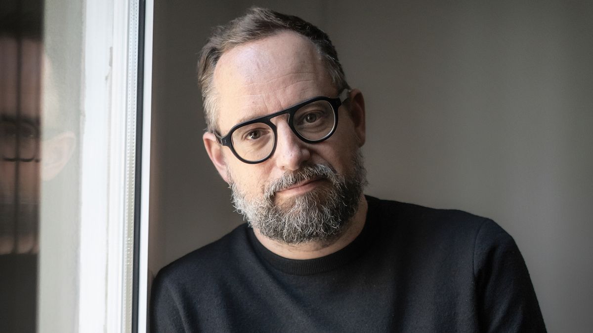 a man with a beard and glasses in a back top looking at the camera