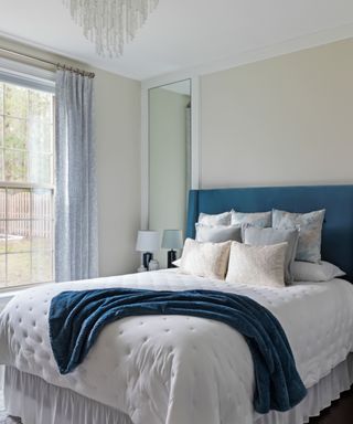 A white and blue bedroom with a blue bed with white bedding and a blue throw