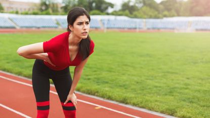 Female runner on running track has side cramps during workout