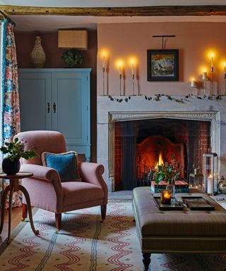 living room with pink armchair and candlesticks on mantlepiece and ottoman and pink painted walls