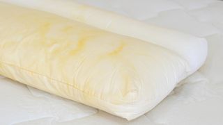 Image shows a white pillow and mattress covered in yellow stains