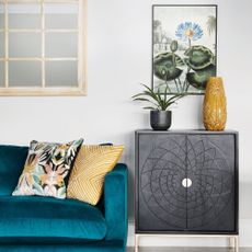 Blue velvet sofa with patterned cushion next to black console and artwork