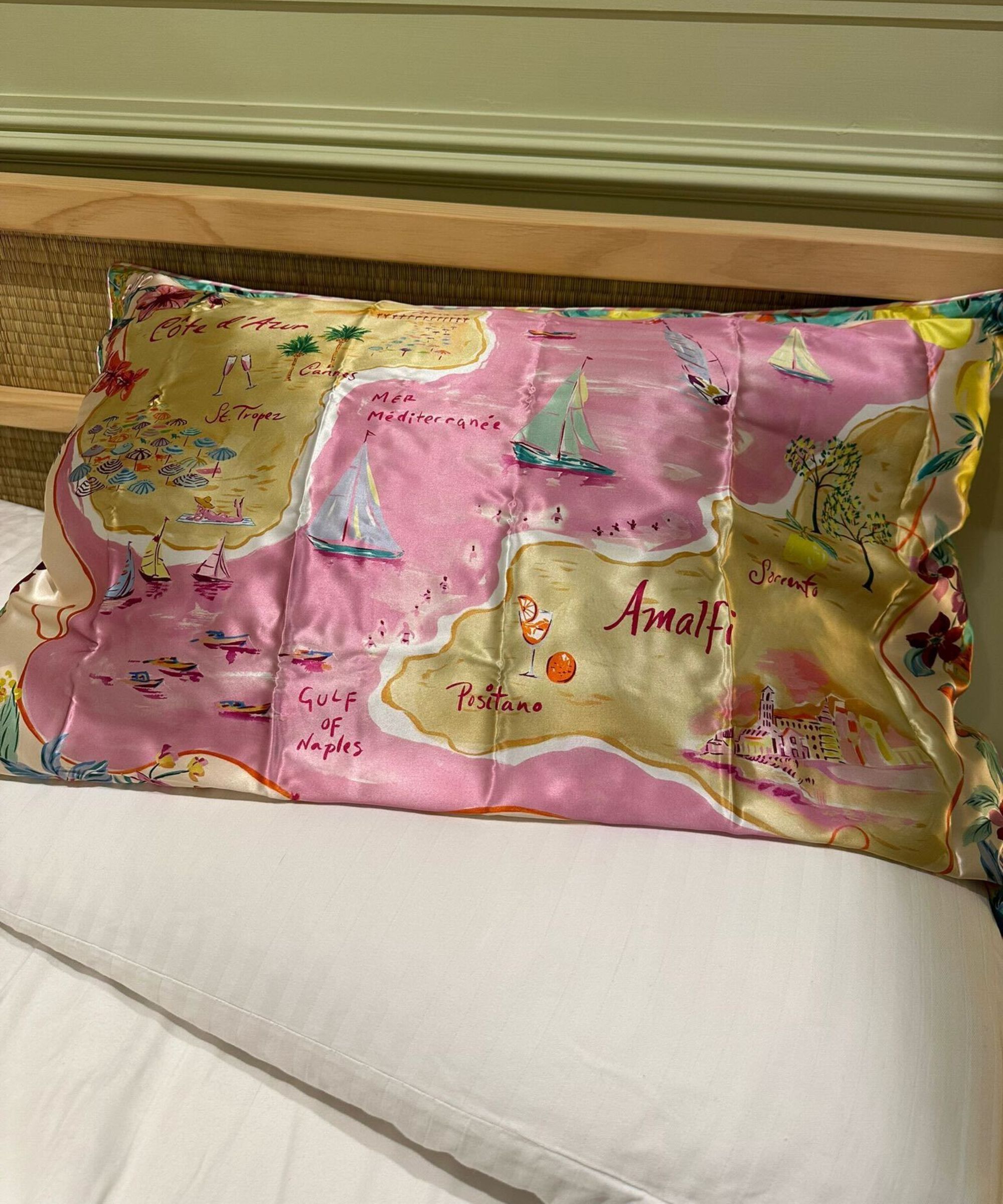 Pink patterned Slip silk pillowcase on white bedding with a rattan Japandi headboard and green wall with panelling behind.