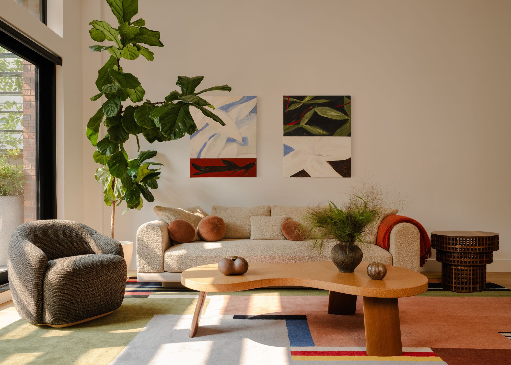 A living room with a multicolored rug, a curving beige sofa and an olive green armchair