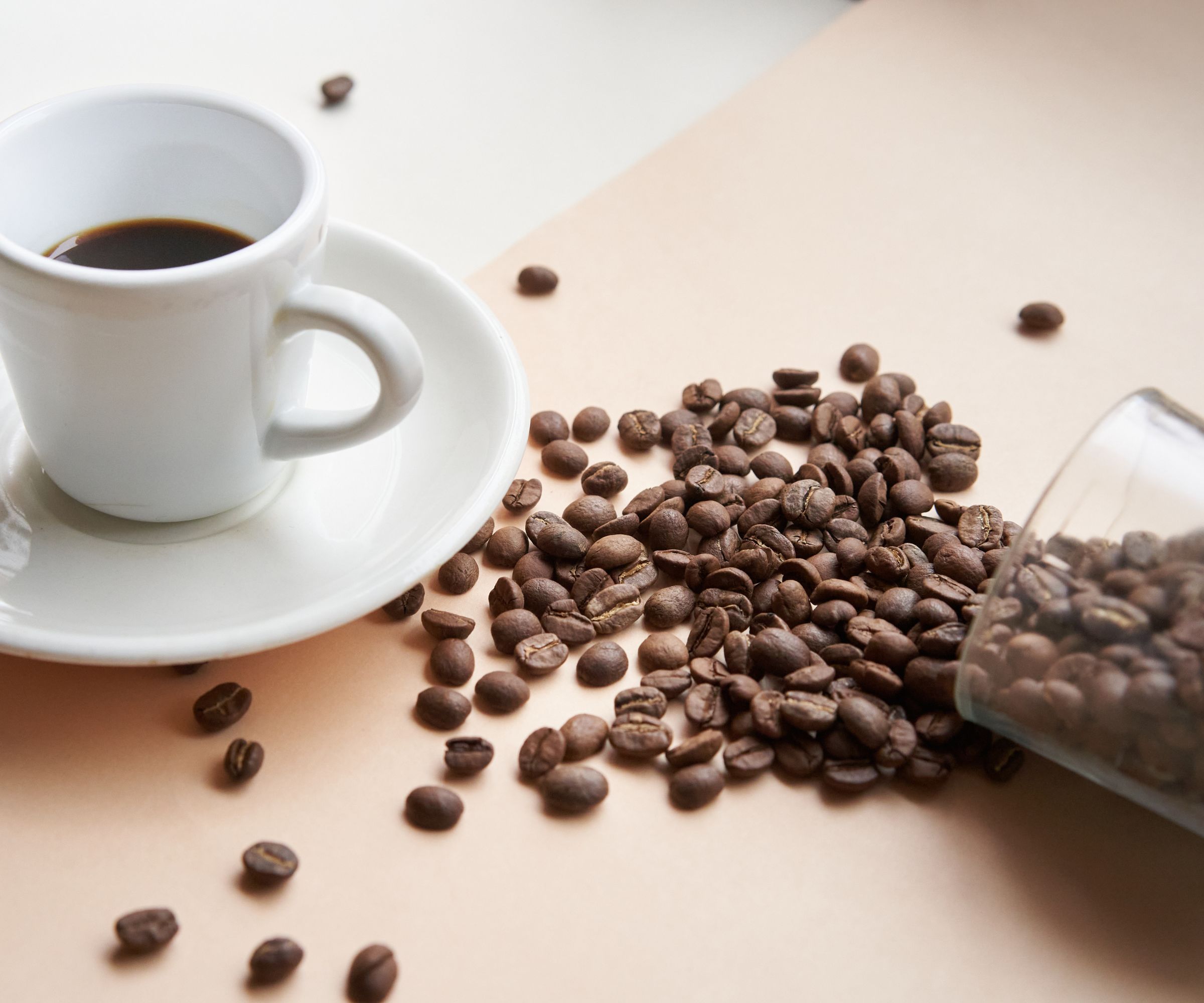 A cup of coffee with beans spilled on the table