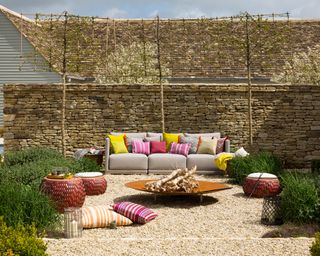 A gravel area with an outdoor sofa with colorful cushions in front of a wall