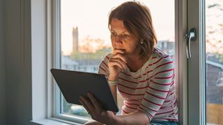 Woman looking stressed, working on laptop, sitting against sun in office window