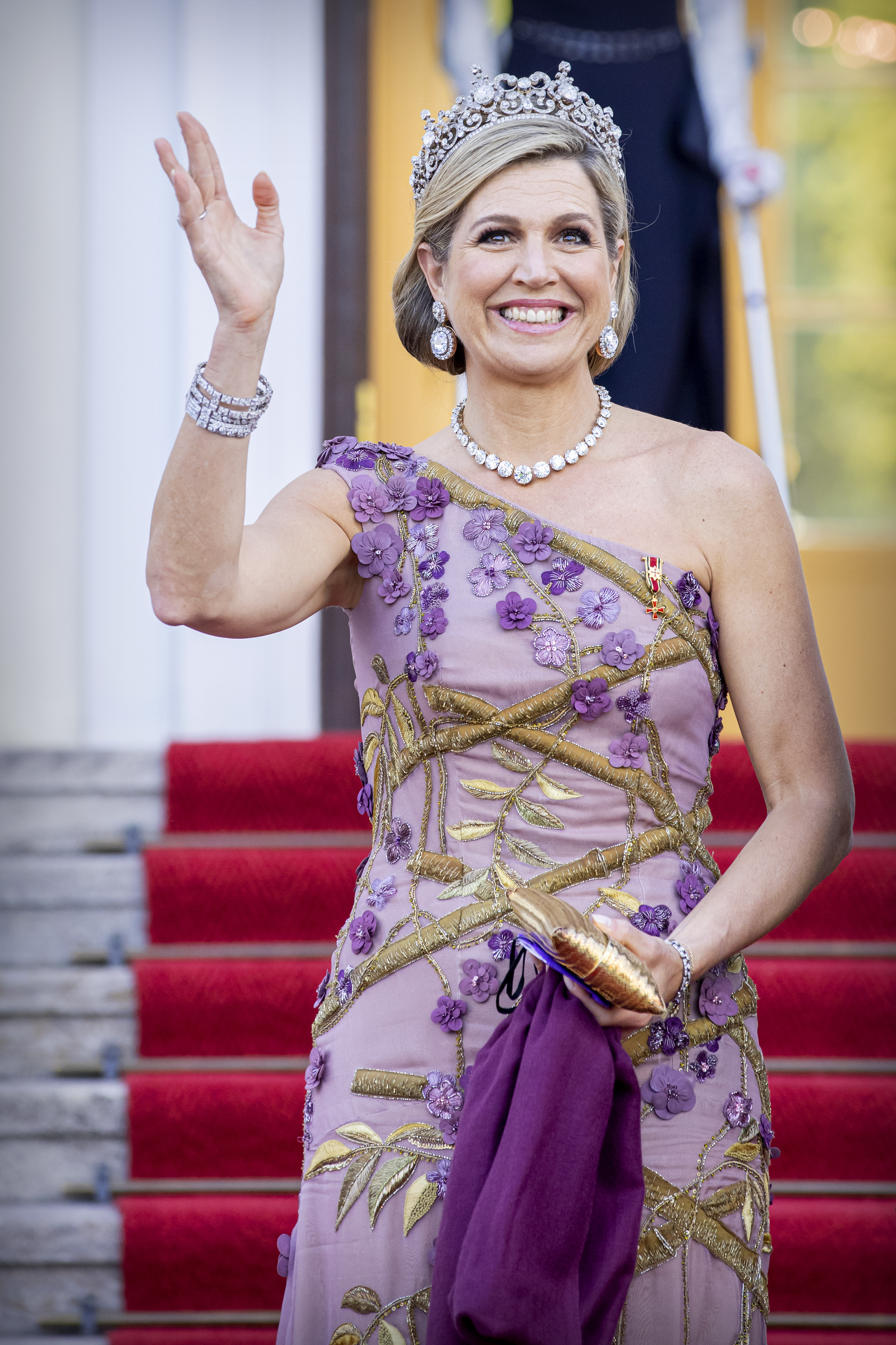 Queen Maxima wearing a tiara and purple gown waving