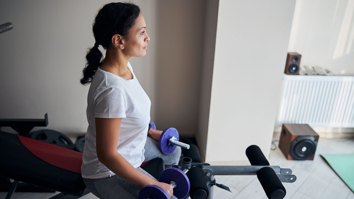 Woman sitting on weights bench holding dumbbells