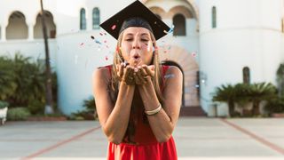 Young female graduate blowing confetti at camera