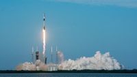 a black-and-white spacex falcon 9 rocket launches into a blue sky.