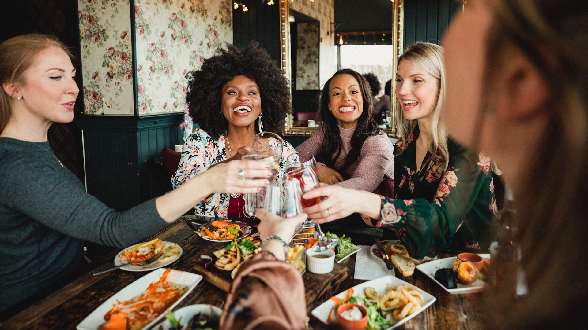 Women clinking glasses to cheers before eating dinner together in a restaurant