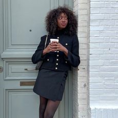 an influencer wears a black cropped jacket and a mini skirt with tights 