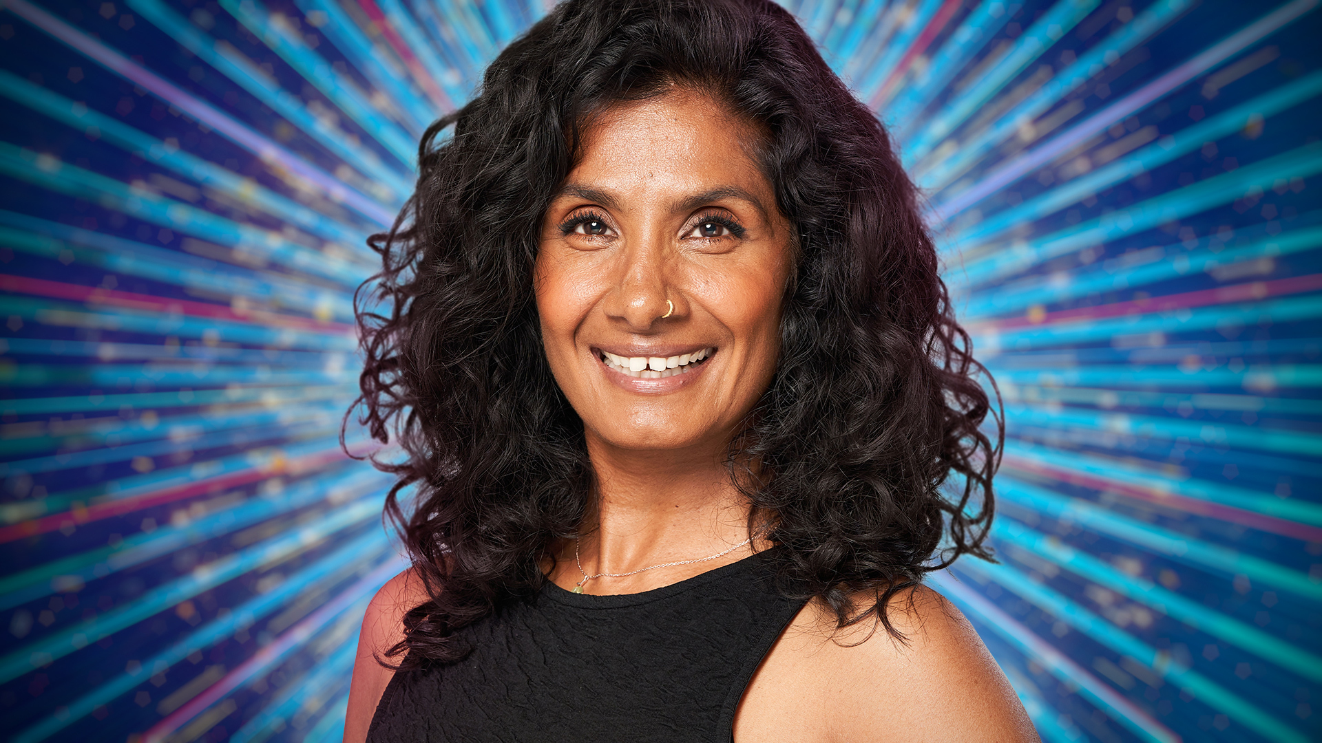 Balvinder Sopal smiling for the camera with a blue sparkly background behind her.