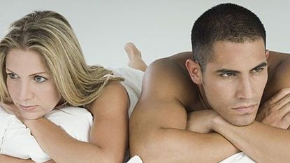 Man and woman lying on white bedsheets, looking disappointed