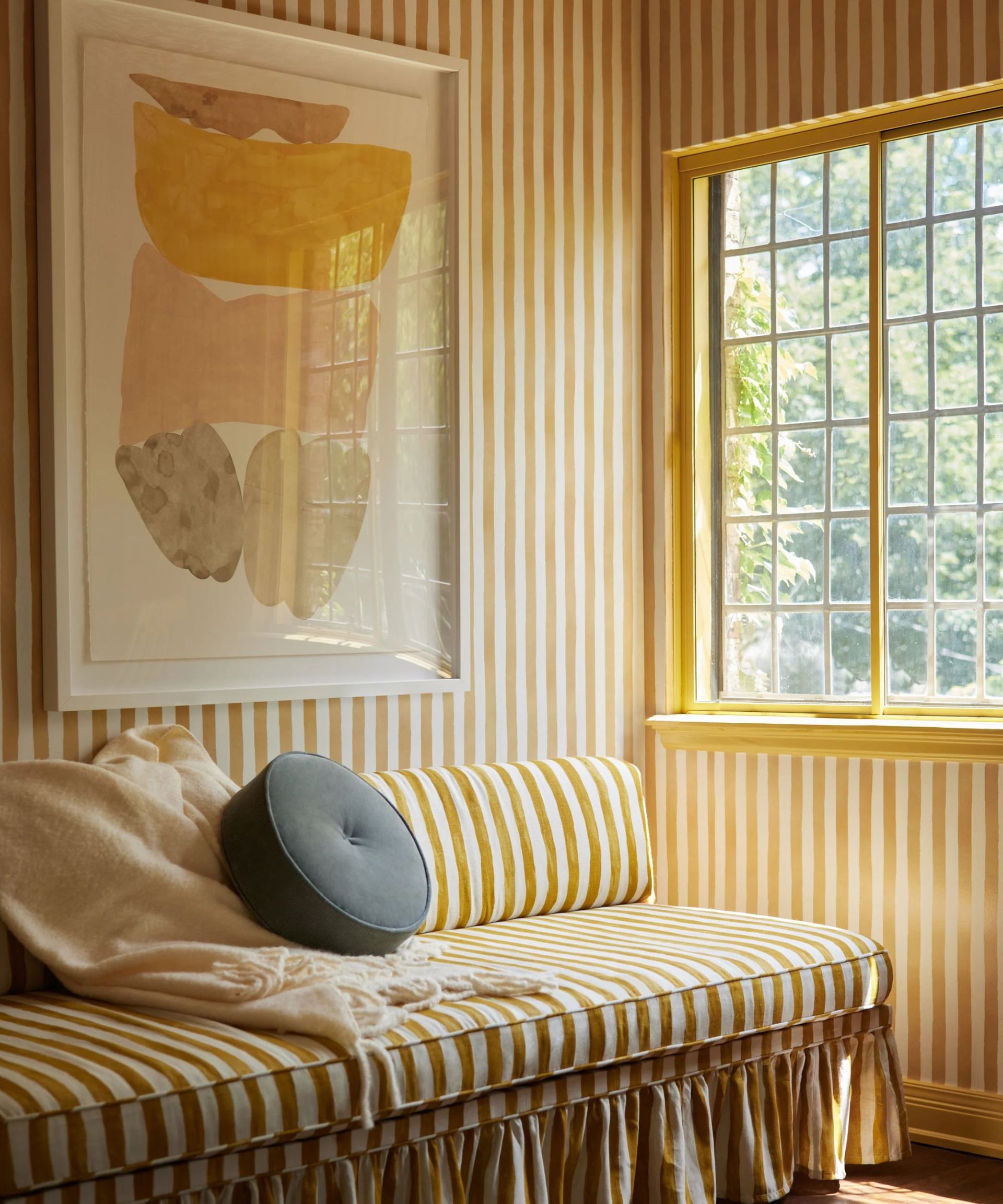 Yellow striped room with matching wallpaper and skirted sofa and yellow window frame