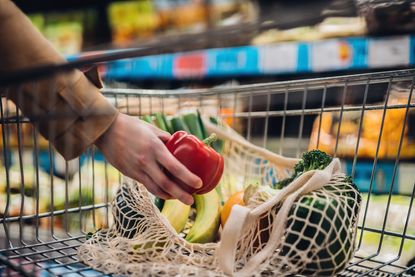 Person putting bell pepper into supermarket basket with other fruit and veg