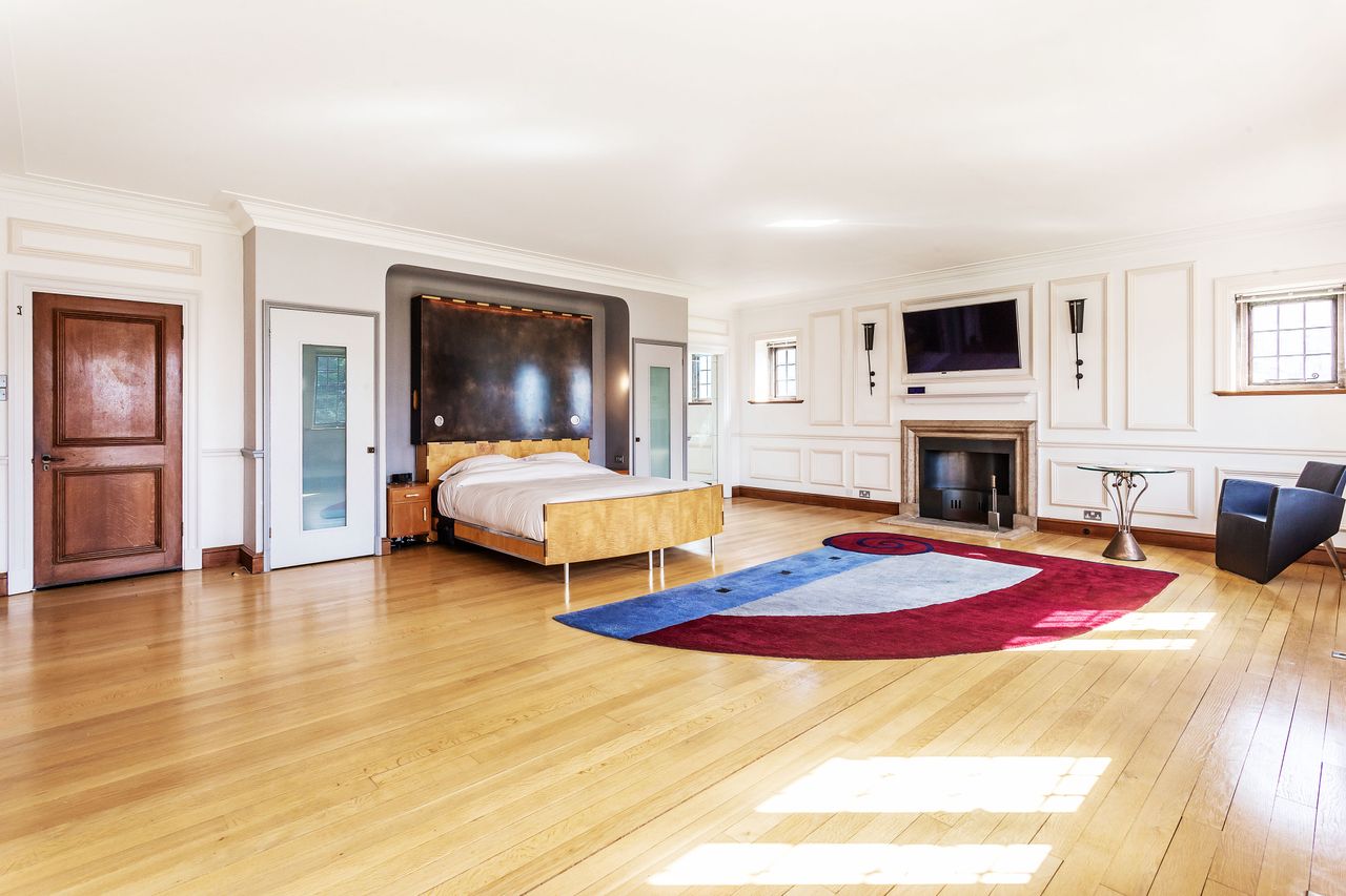 A large bedroom with a wooden floor and fireplace and wall mounted TV