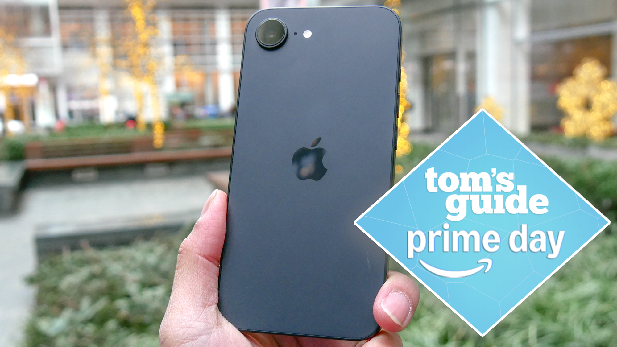 iPhone 16e in the hand with a Tom&#039;s Guide deal badge on top
