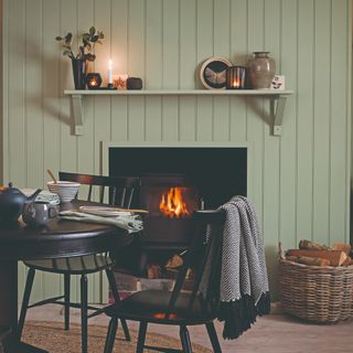 A fireplace with a wood-panelled surround painted a sage green with a floating shelf used as a mantelpiece